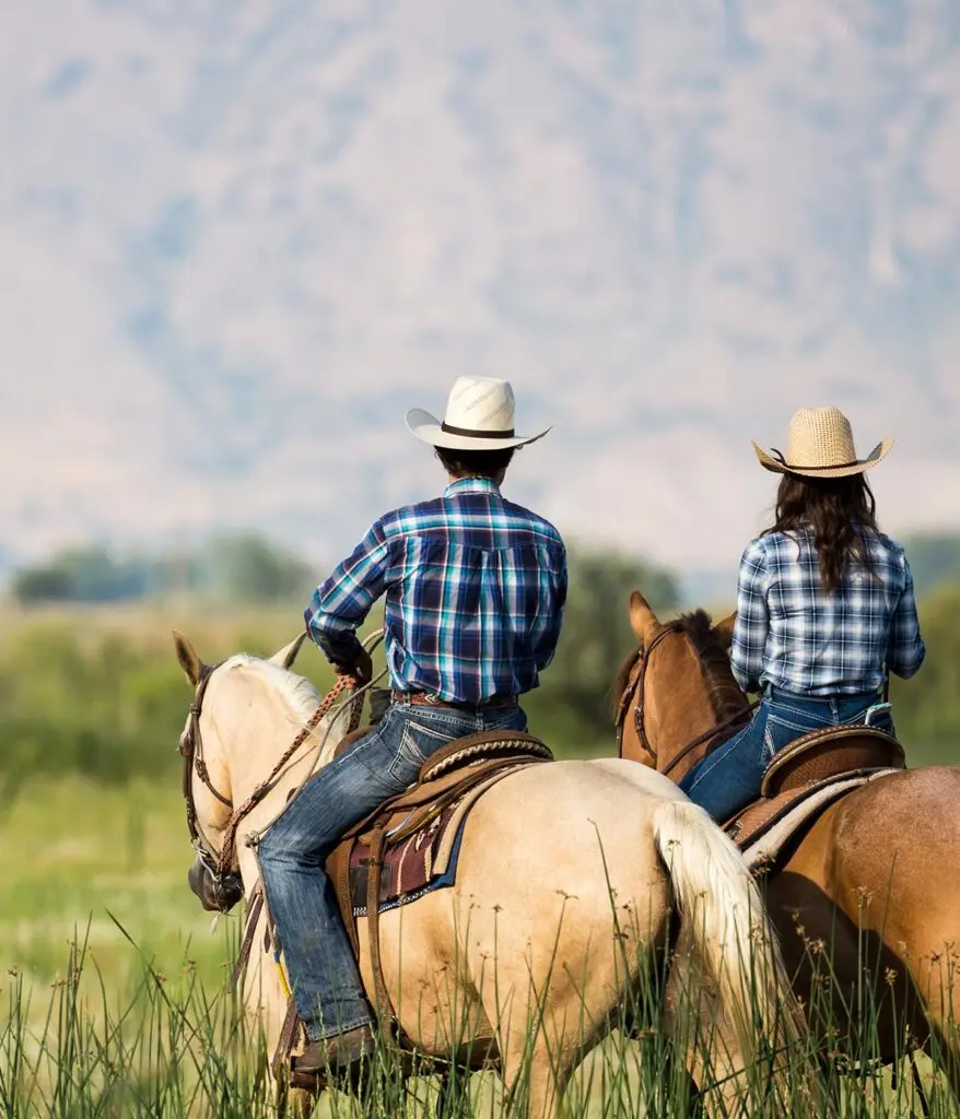 Two people with cowboy hats on horses